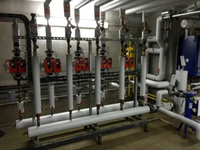 Salle technique avec réseau complexe de tuyauterie industrielle en PVC et métal, incluant vannes et pompes pour le chauffage et la climatisation.