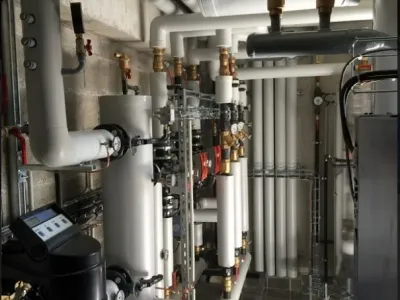 Installation industrielle de conduits et pompes dans une salle technique, avec tuyauterie isolée et raccords pour fluides techniques.