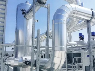 Réseau de conduits métalliques sur toiture industrielle, formant un système HVAC avec supports et coudes.
